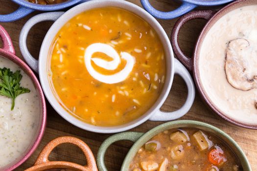 Overhead view of assorted soup in bowls with handles with focus to a cup of chicken broth with wild rice garnished with a twirl of sour cream