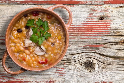 Bean and barley soup garnished with fresh sliced mushrooms and a sprig of parsley served in a bowl on a rustic wooden table with copy space, overhead view