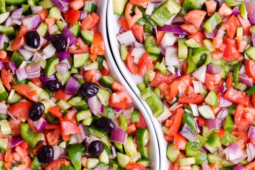Fresh colorful Turkish shepherd salad with diced tomato, onion and sweet pepper served with and without olives in a divided dish, close up full frame background view from above