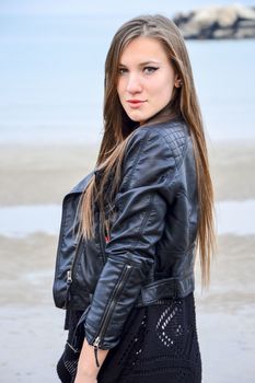 Beautiful girl in a fur coat and hat against the sea in autumn day.