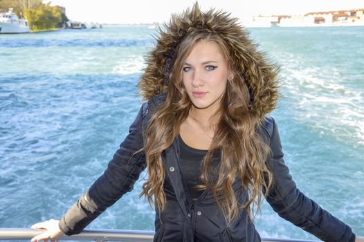 Beautiful girl in a fur coat and hat against the sea in autumn day.