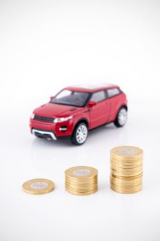 Saving money to buy a vehicle. Coins and car toy on white