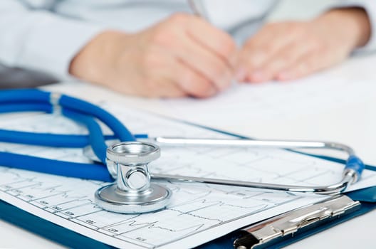 Medical doctor working at desk. Close up of stethoscope in foreground