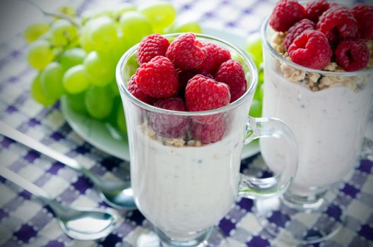 Glass of dessert with yoghurt, fresh berries and muesli. Grapes in background