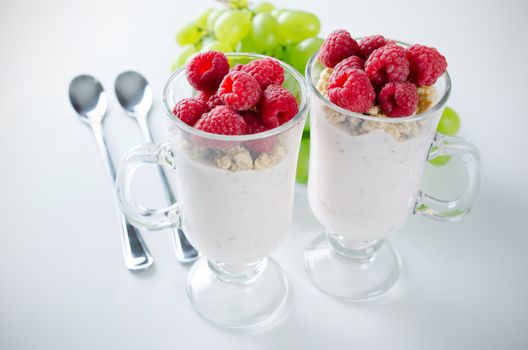 Glass of dessert with yoghurt, fresh berries and muesli. Grapes in background