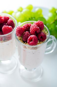 Glass of dessert with yoghurt, fresh berries and muesli. Grapes in background