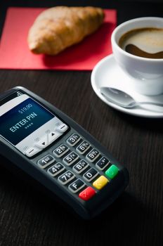 Payment terminal in restaurant. Croissaint and coffee in background