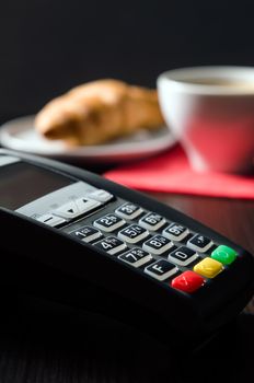 Payment terminal in restaurant. Croissaint and coffee in background