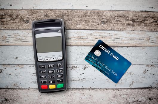 Payment terminal and credit card on wooden background top view