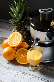 Juicer and orange juice in glass on wooden desk. Fruits in background