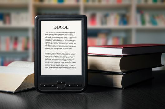 E-book reader device on desk in library. Alternative for traditional books