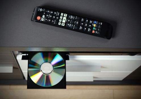 Remote control and Blu-ray or DVD player with inserted disc. 