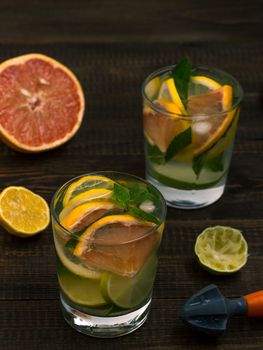 Cold homemade lemonade with fresh lemon, lime, grapefruit and mint by lemon reamer. Summer drink on dark wooden background. Vertical