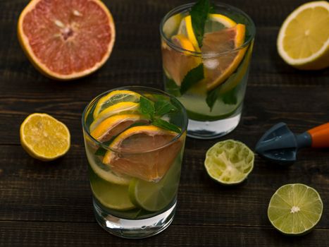 Cold homemade lemonade with fresh lemon, lime, grapefruit and mint by lemon reamer. Summer drink on dark wooden background