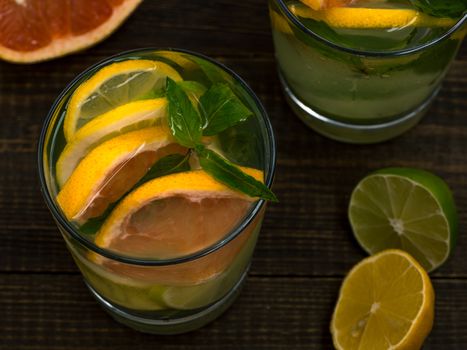 Closeup cold homemade lemonade with fresh lemon, lime, grapefruit and mint. Summer drink on dark wooden background