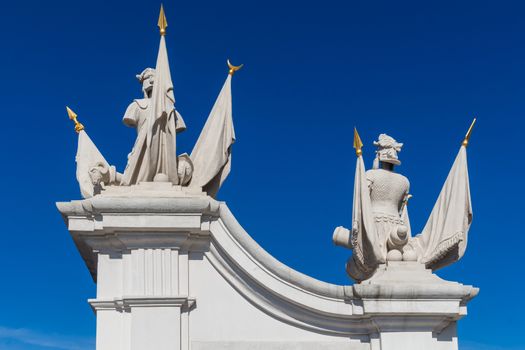 Detail of a gate at the castle in Bratislava, Slovakia, which is part of UNESCO World Heritage site. Statues with flags. Bright blue summer sky.