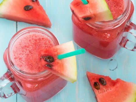 Watermelon smothie and slices on soft blue wooden background