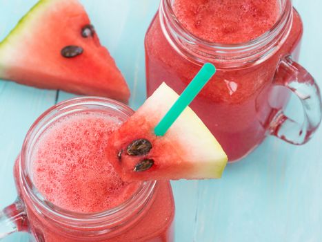 Watermelon smothie and slices on soft blue wooden background