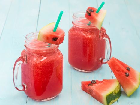 Watermelon smothie and slices on soft blue wooden background