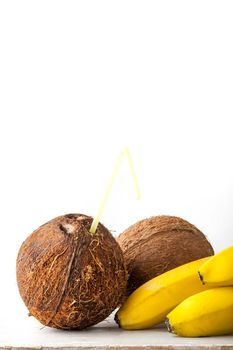 Coconut with straw and bananas on the white table vertical