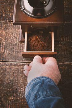 Coffee mill with hand on the wooden table vertical