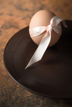 Egg with ribbon on the brown plate vertical
