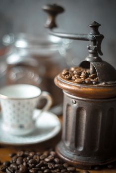 Coffee mill with coffee beans and blurred cup vertical