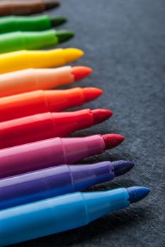 Colorful felt pens on the dark stone background vertical