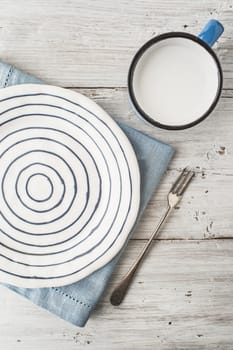 Ceramic plate with fork and cup of milk on the wooden table vertical