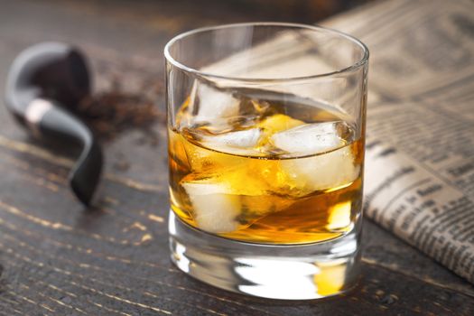 Whiskey with ice  and blurred pipe and newspaper