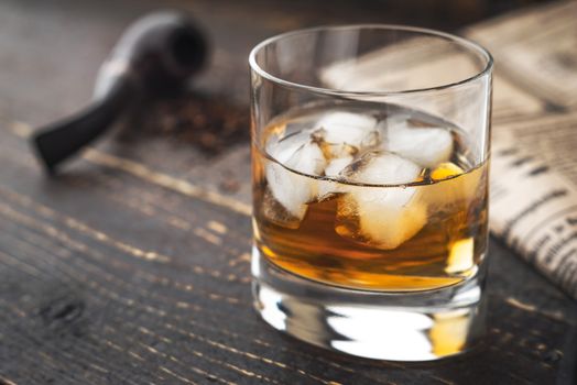 Whiskey with ice  and blurred pipe and newspaper horizontal