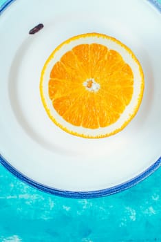 Half of orange on the white plate on the cyan background vertical