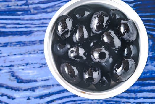 Black olives in the bowl on the blue background top view