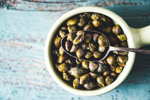 Capers in the bowl on the light blue background top view