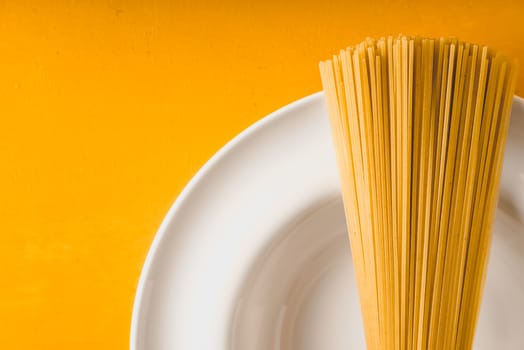 Raw spaghetti  on the white plate on the yellow background