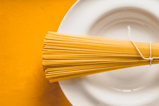 Raw spaghetti  on the white plate on the yellow background horizontal
