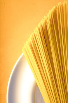 Raw spaghetti  on the white plate on the yellow background vertical