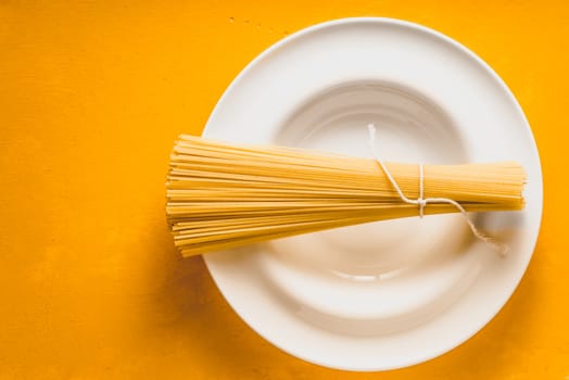 Raw spaghetti  on the white plate on the yellow background top view