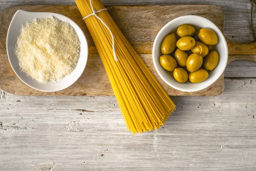 Raw spaghetti with olives and cheese on the white wooden table top view