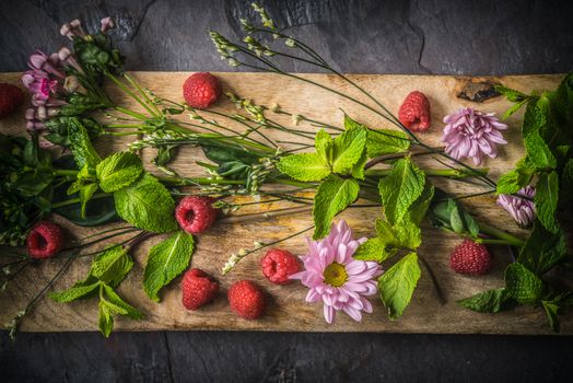 Flowers  , raspberries and mint on the wooden board  top view