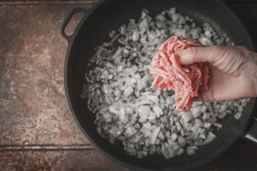 Raw minced meat in the hand with blurred pan top view