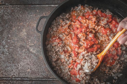 Fried minced meat with onion and chopped tomatoes in the pan on the metal background