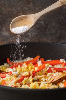 Adding salt in the pan with rice and bell pepper vertical