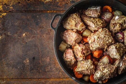 Meat with vegetables in the pan on the metal background