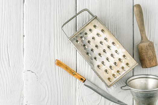 Grater, plunger , strainer and knife on the white wooden table top view