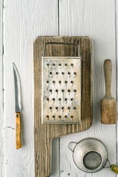 Grater, plunger , strainer and knife on the white wooden table vertical