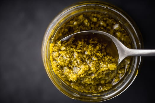 Pesto sauce in the glass jar with spoon top view