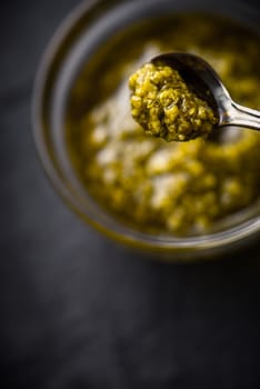 Pesto sauce in the metal spoon with blurred jar vertical