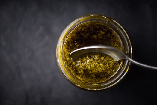 Pesto sauce in the glass jar with spoon horizontal