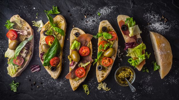 Slices of ciabatta with olives , tomatoes and basil on the black stone table wide screen